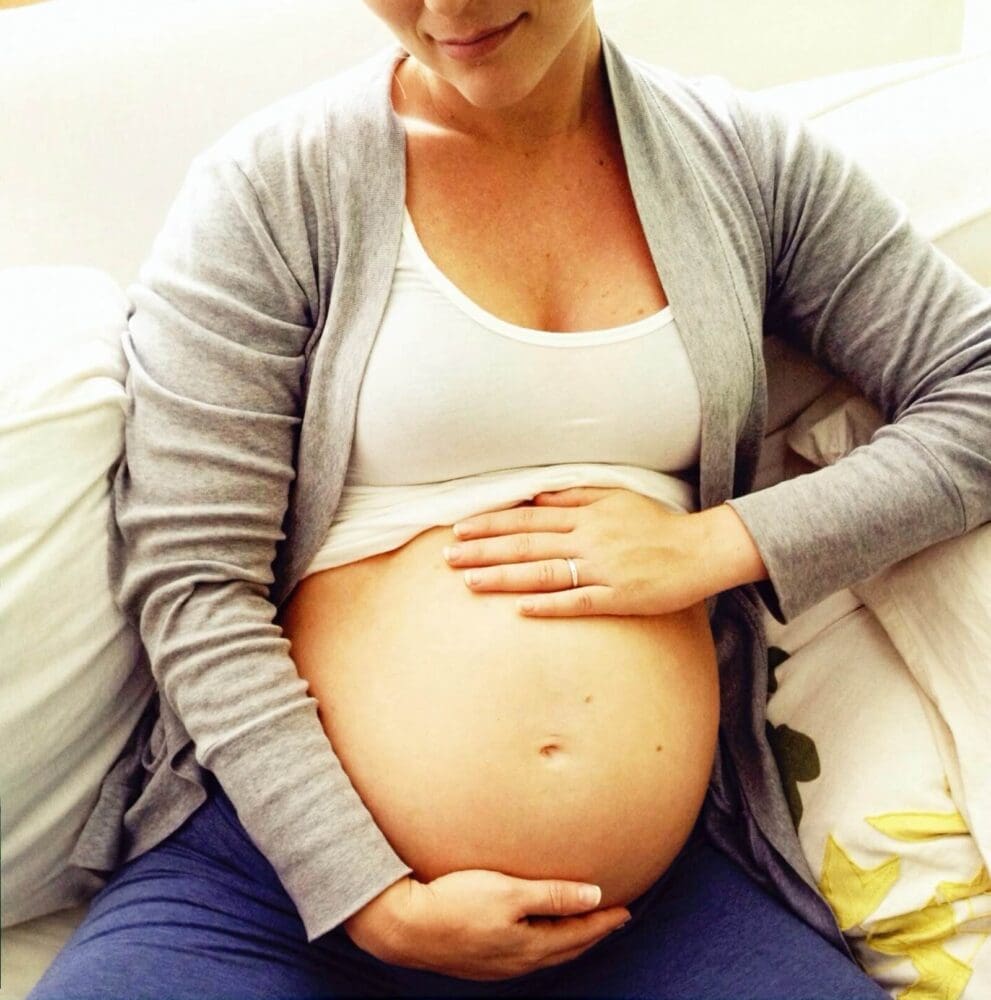 Pregnant woman sitting down with her shirt pulled up and hands on belly