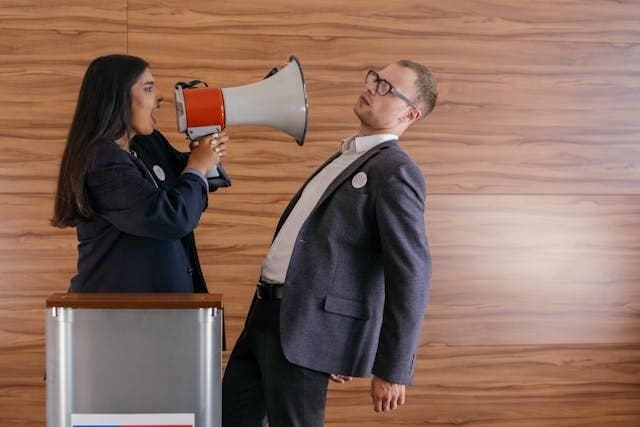 Voting against their own best interests. A female politician yells into a bullhorn in the face of her opponent.