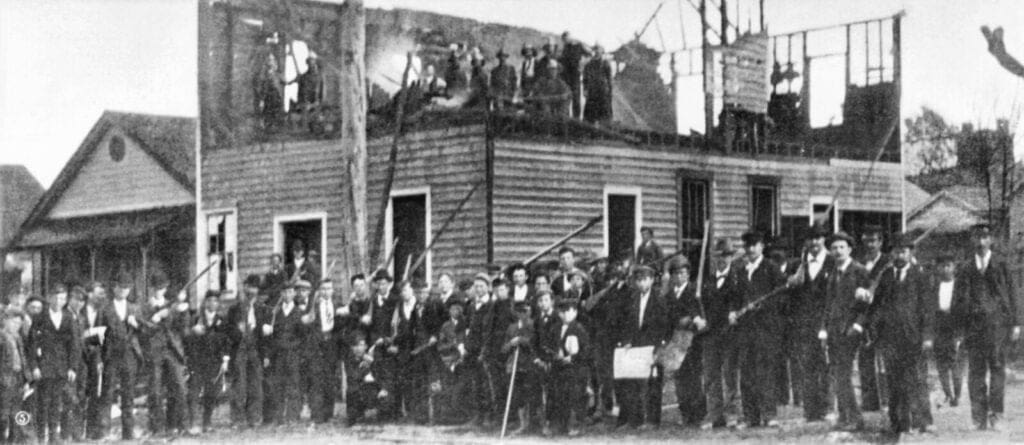 Wilmington Massacre Wilmington, N.C. race riot, 1898: Armed rioters in front of the burned-down "Record" press building.